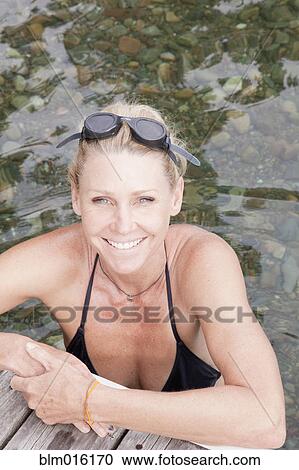 Stock Image - Caucasian woman in lake leaning on pier. Fotosearch