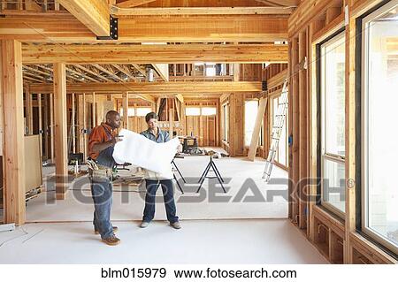 Stock Photo - Construction workers looking at blueprints in unfinished room. Fotosearch