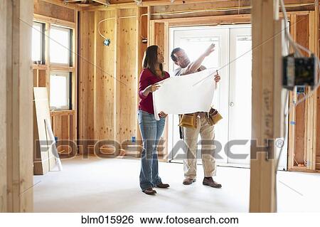 Stock Photograph - Construction workers looking at blueprints in unfinished room. Fotosearch