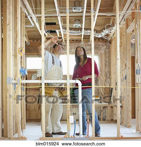 Picture - Construction workers looking at wiring in unfinished room. Fotosearch