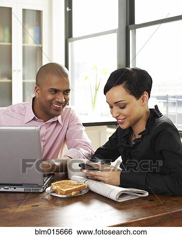Stock Photograph - Couple eating breakfast and using laptop and cell phone. Fotosearch