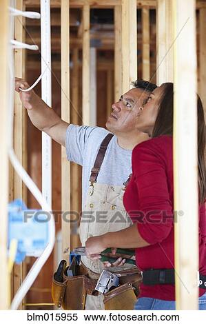 Stock Photography - Electricians looking at wiring in unfinished room. Fotosearch