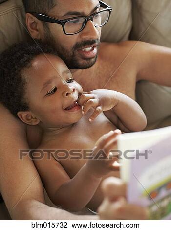 Stock Image - Father reading book to African American baby. Fotosearch