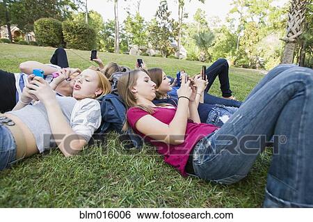 Stock Photograph - Friends hanging out together on grass using cell phones. Fotosearch