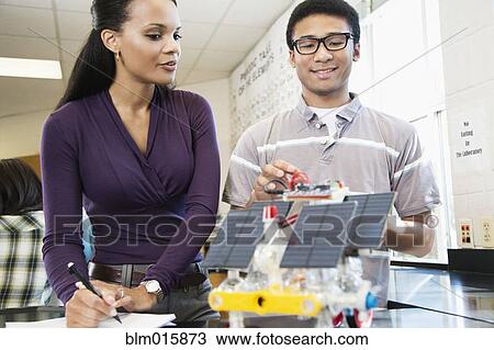 Stock Image - High school student and teacher working on solar powered machine in classroom. Fotosearch