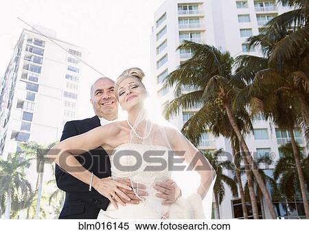Stock Photography - Hispanic bride in groom hugging outdoors. Fotosearch