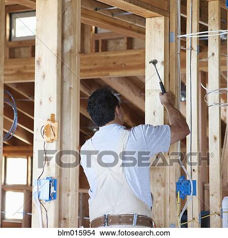 Hispanic carpenter hammering wall frame in unfinished room View Large Photo Image Picture - Hispanic carpenter hammering wall frame in unfinished room. Fotosearch