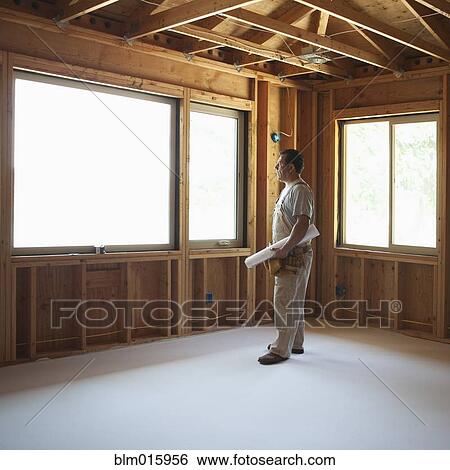 Hispanic construction worker holding blueprints in unfinished room View Large Photo Image Stock Photograph - Hispanic construction worker holding blueprints in unfinished room. Fotosearch