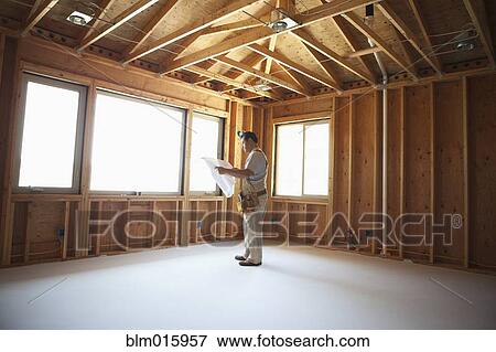 Hispanic construction worker looking at blueprints in unfinished room View Large Photo Image Stock Photo - Hispanic construction worker looking at blueprints in unfinished room. Fotosearch