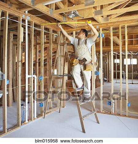 Hispanic construction worker measuring ceiling in unfinished room View Large Photo Image Stock Photo - Hispanic construction worker measuring ceiling in unfinished room. Fotosearch