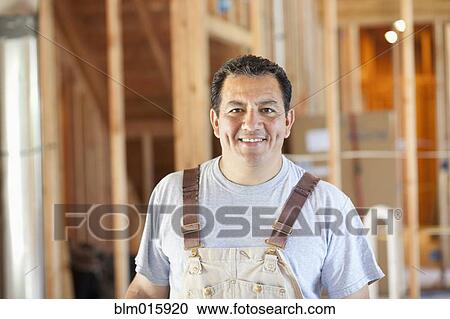 Stock Image - Hispanic construction worker standing in unfinished room. Fotosearch