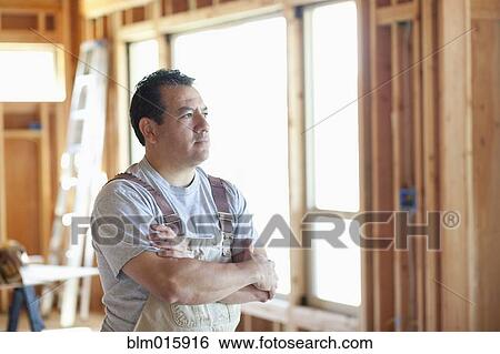 Stock Photograph - Hispanic construction worker standing in unfinished room. Fotosearch