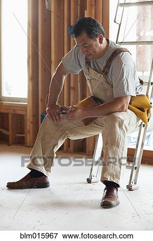 Hispanic construction worker text messaging on cell phone in unfinished room View Large Photo Image Stock Photo - Hispanic construction worker text messaging on cell phone in unfinished room. Fotosearch