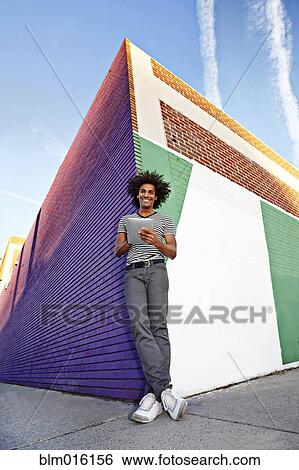 Stock Photograph - Man using digital tablet and leaning on wall outdoors. Fotosearch