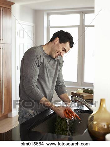 Picture - Man washing carrots and talking on telephone. Fotosearch