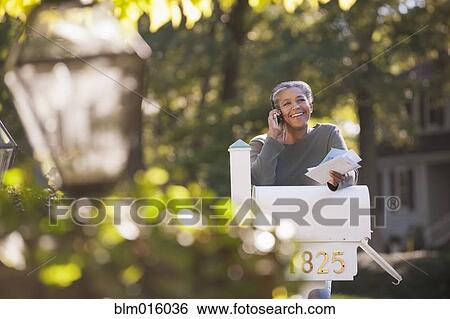Mixed race woman holding mail and talking on cell phone View Large Photo Image Stock Photograph - Mixed race woman holding mail and talking on cell phone. Fotosearch