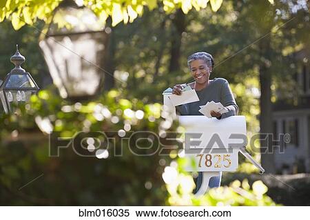 Stock Photography - Mixed race woman reading mail at mailbox. Fotosearch