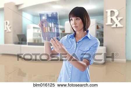 Stock Photography - Mixed race woman using digital tablet in pharmacy. Fotosearch