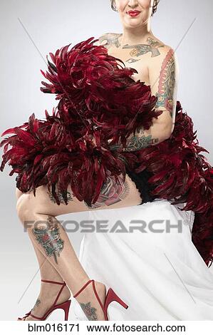 Stock Image - Mixed race woman with tattoos covered with feather boa. Fotosearch