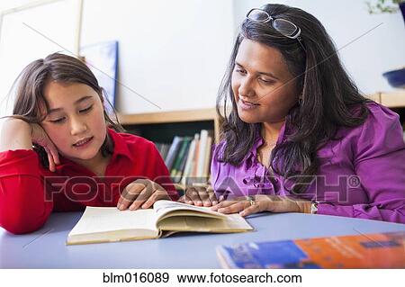 Stock Photo - Teacher and student reading book in classroom. Fotosearch