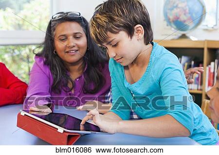 Stock Photograph - Teacher and student using digital tablet in classroom. Fotosearch