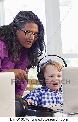Stock Image - Teacher helping student using laptop. Fotosearch