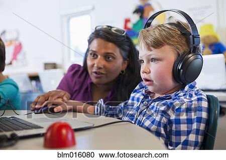 Stock Image - Teacher helping student using laptop. Fotosearch