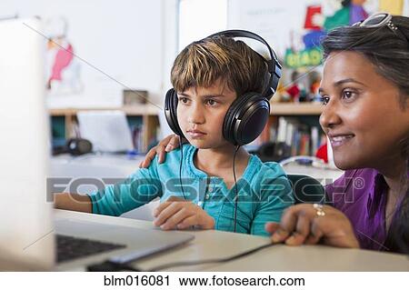 Stock Image - Teacher helping student using laptop. Fotosearch