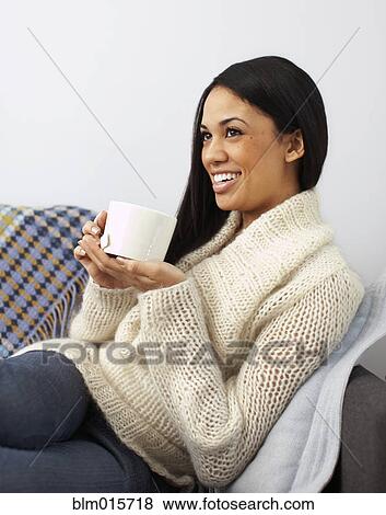 Stock Photo - Woman sitting on sofa drinking coffee. Fotosearch