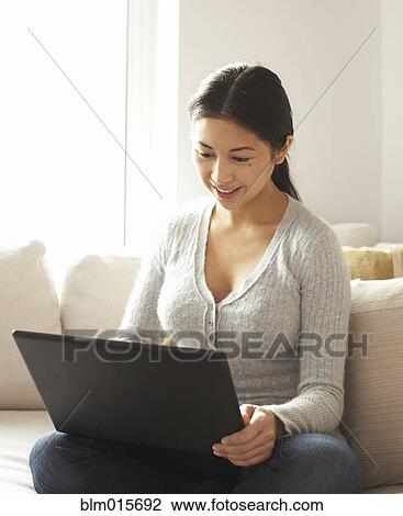 Stock Image - Woman sitting on sofa using laptop. Fotosearch