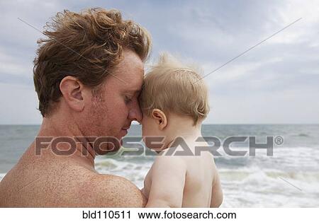 Stock Image - Caucasian father holding baby on beach. Fotosearch