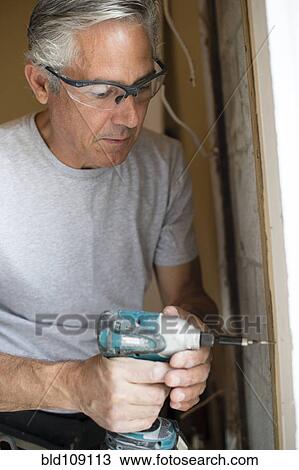 Stock Image - Caucasian man using power drill. Fotosearch