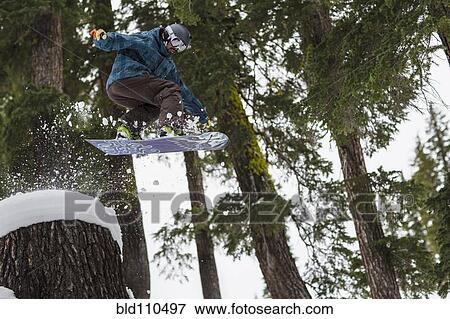 Stock Photo - Caucasian snowboarder jumping on snowy slope. Fotosearch