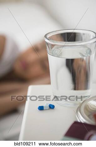 Stock Image - Close up of pills and water on bedside table. Fotosearch