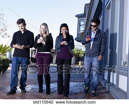Friends using cell phones outdoors View Large Photo Image Stock Image - Friends using cell phones outdoors. Fotosearch