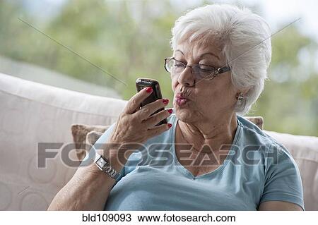 Stock Image - Hispanic woman making kissy face at cell phone. Fotosearch