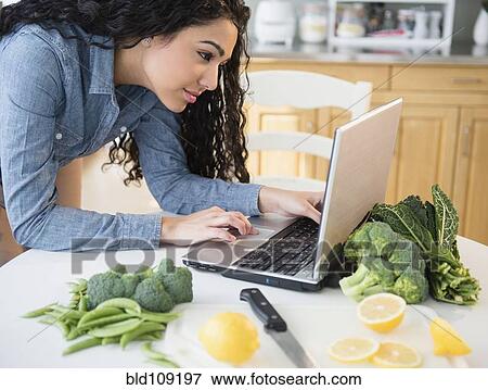 Stock Photo - Hispanic woman using laptop to cook. Fotosearch