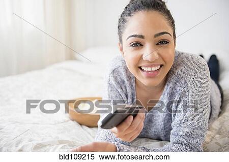 Stock Photography - Hispanic woman watching television on bed. Fotosearch
