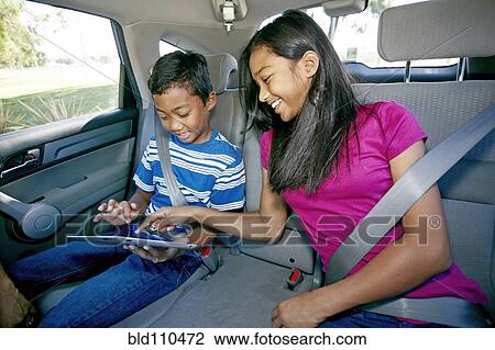 Stock Image - Mixed race children using digital tablet in car. Fotosearch