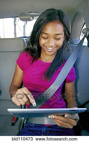Stock Image - Mixed race girl using digital tablet in car. Fotosearch
