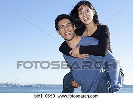 Stock Image - Mixed race man carrying girlfriend piggy back. Fotosearch
