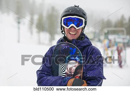 Stock Image - Mixed race snowboarder standing in snow. Fotosearch