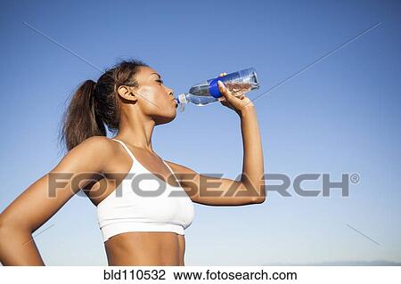 Stock Image - Mixed race woman drinking water bottle. Fotosearch