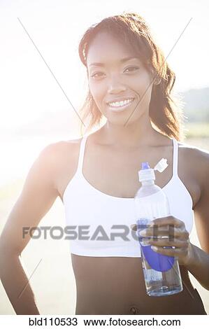 Stock Image - Mixed race woman drinking water bottle. Fotosearch