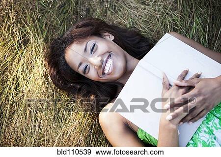 Stock Photo - Mixed race woman holding book in grass. Fotosearch