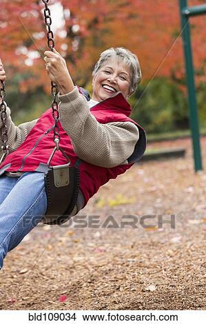 Picture - Mixed race woman on swing in park. Fotosearch