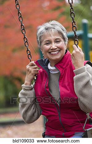 Stock Image - Mixed race woman on swing in park. Fotosearch