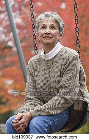 Stock Photo - Mixed race woman on swing in park. Fotosearch