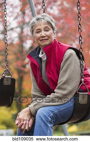 Stock Photography - Mixed race woman on swing in park. Fotosearch