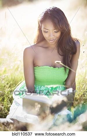 Stock Photo - Mixed race woman reading in grass. Fotosearch